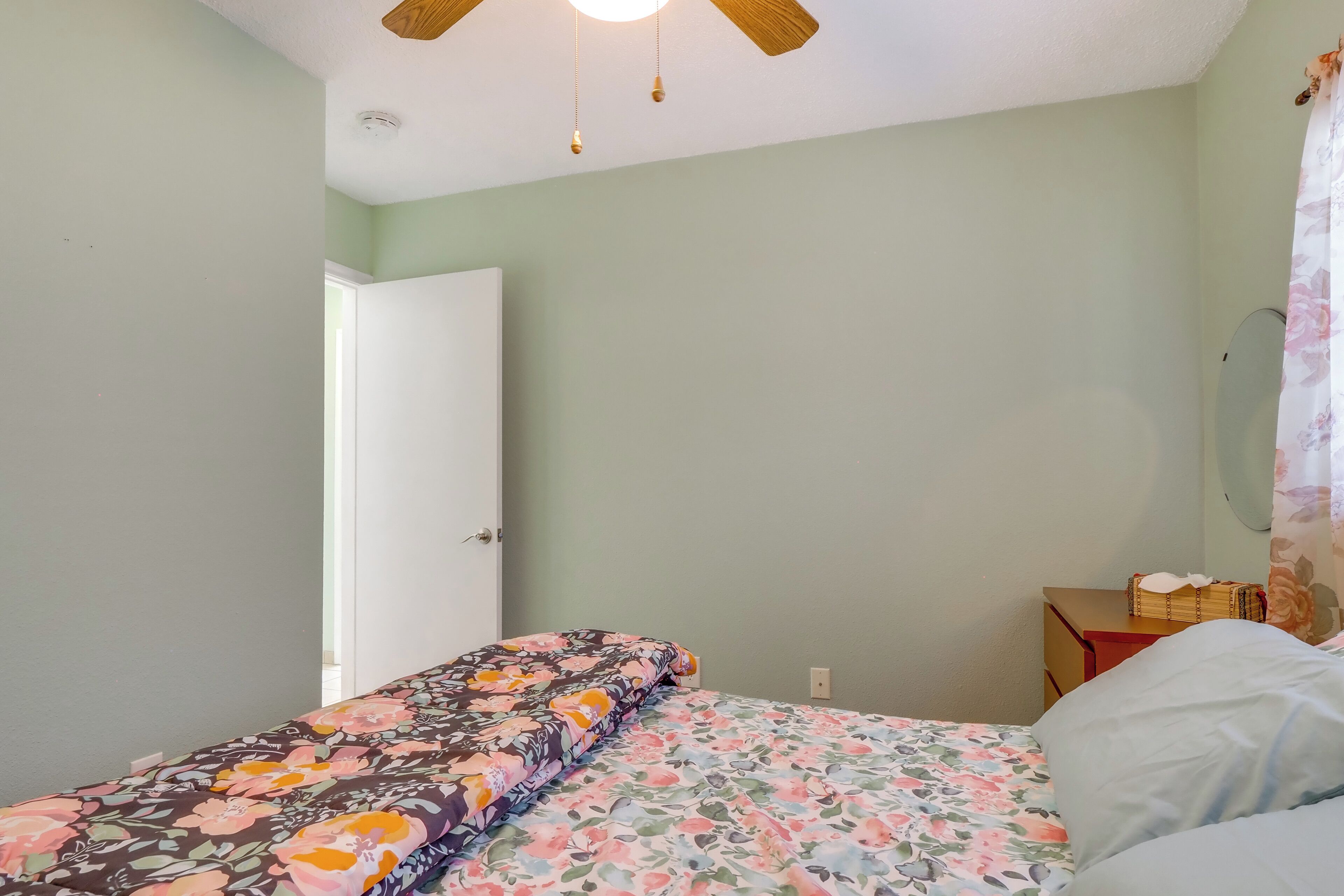 A bedroom with a bed, a nightstand, a ceiling fan, and a door leading to another room.