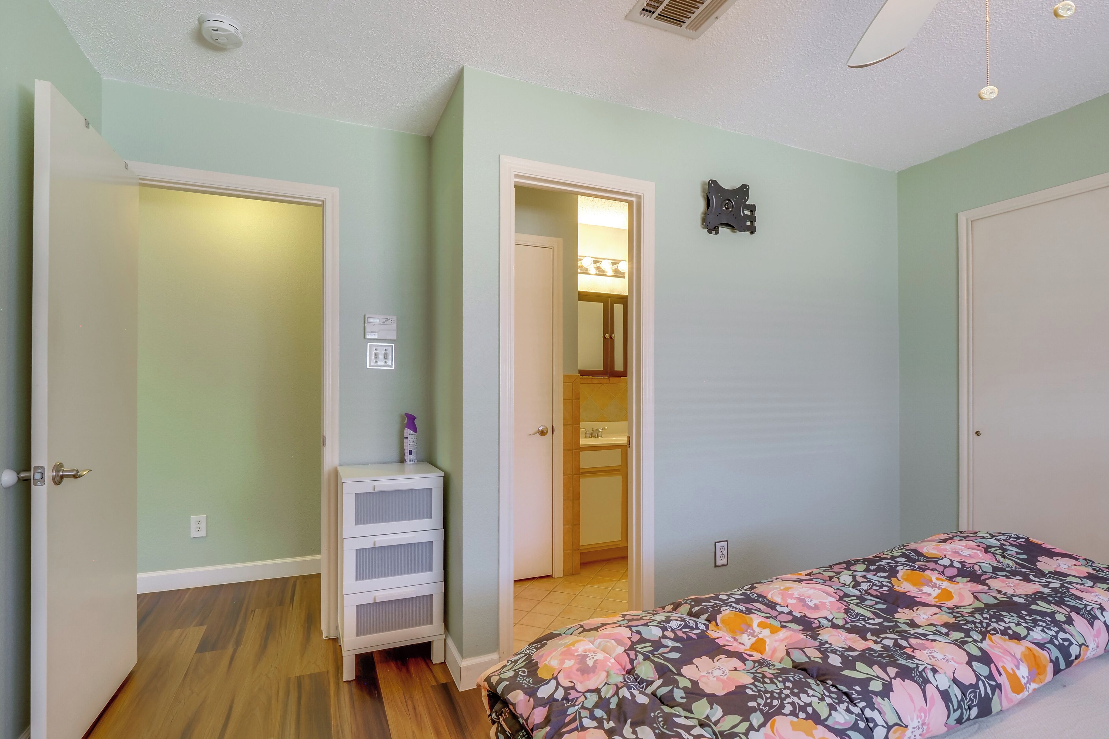 A bedroom with a bed, a wardrobe, a small cabinet, and a door leading to a bathroom.