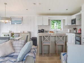 A modern kitchen with white cabinets, a stainless steel microwave, and a window with a view of greenery. - Edmonton Lodge - UK50308 (Doublebois, near Liskeard)