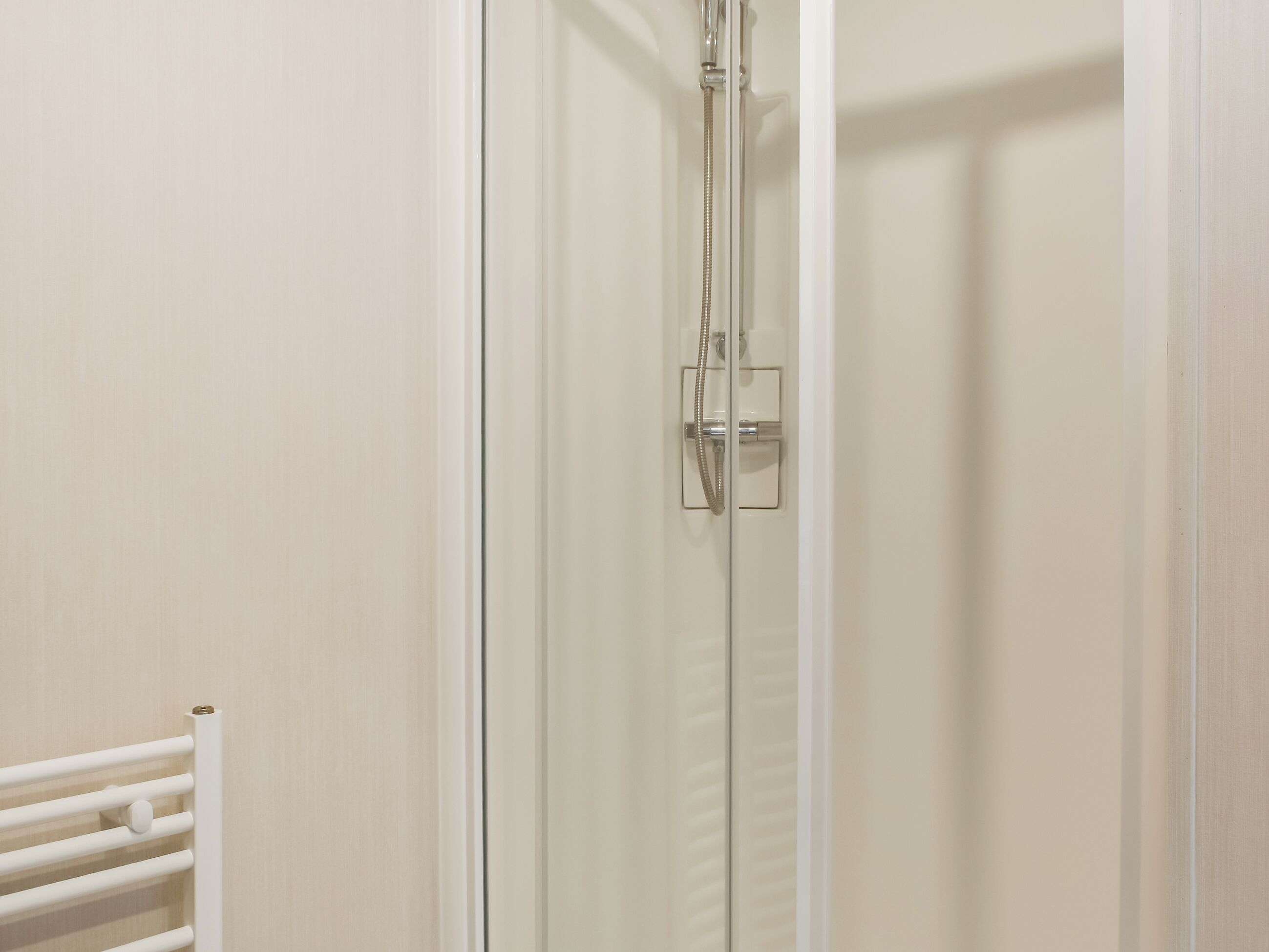 Une douche avec une porte en verre, un porte-serviettes blanc et un panneau de commande.