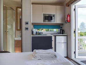 A compact hotel room with a kitchenette, a bed with neatly folded white towels, and a view of greenery through the window. - Valley View - UK50320 (Liskeard)