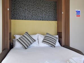 Un lit bien fait, agrémenté de deux coussins à motifs, d’une tête de lit en bois et d’un panneau décoratif mural.