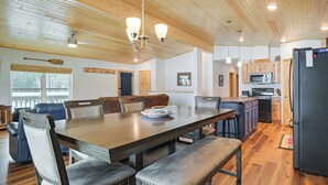 Un comedor amplio con una mesa y sillas de madera, una araña y una cocina con electrodomésticos modernos.