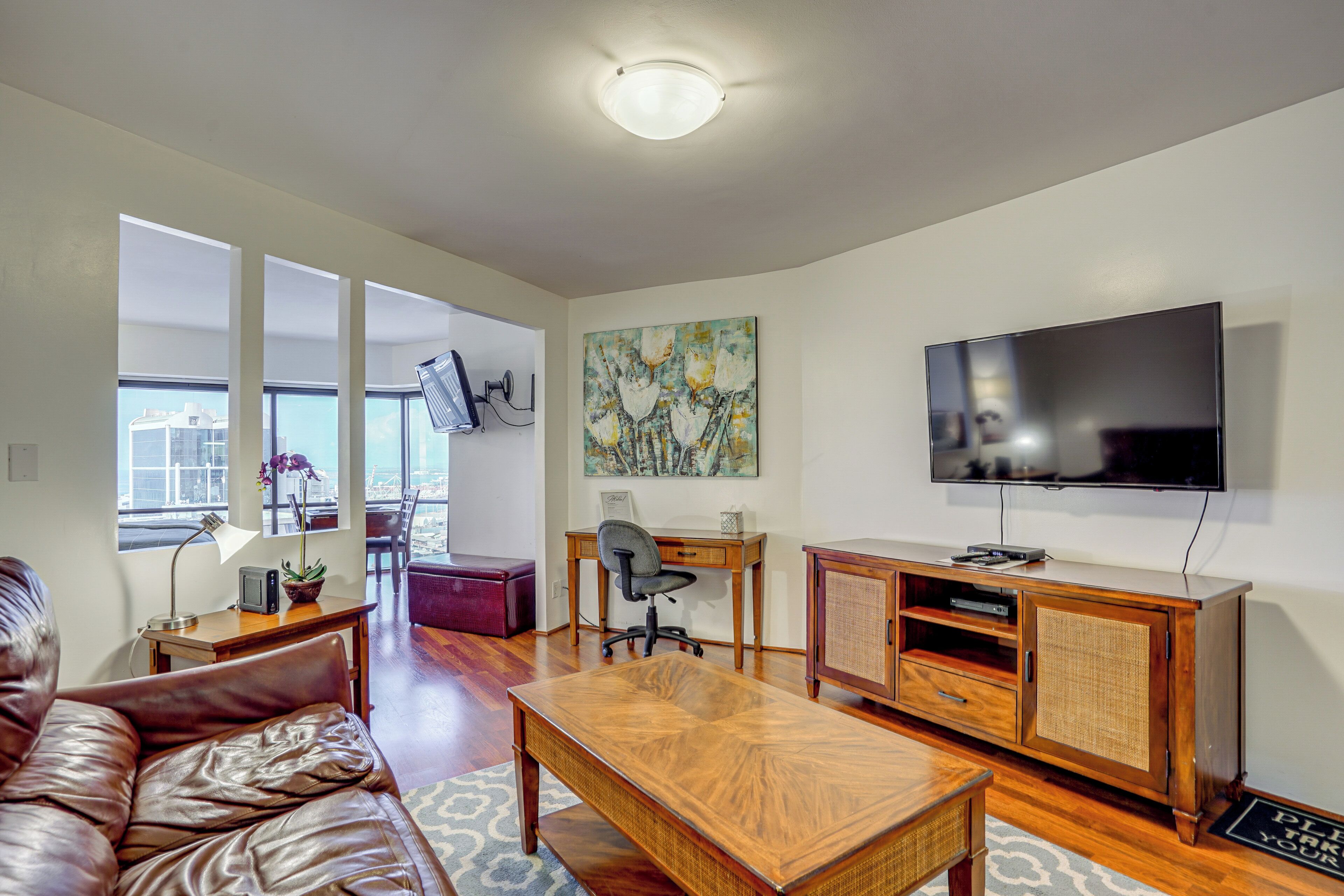 A modern living room with a leather sofa, wooden coffee table, and a TV on the wall.