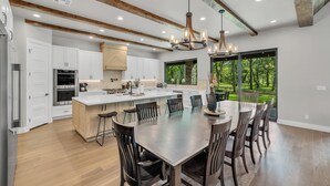 Une cuisine spacieuse dotée d’un grand îlot central, de poutres en bois et offrant une vue sur l’extérieur.