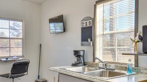 Una cocina con un lavamanos, una cafetera, un calendario y un ventanal con persianas.