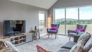 A modern living room with a flat-screen TV, two grey armchairs with purple cushions, a grey sofa, and a wooden coffee table. - 4 bedroom accommodation in Blackwaterfoot (Blackwaterfoot)