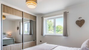 A bedroom with a large mirror, a bed with white bedding, a window with curtains, and a wall-mounted heart decoration. - 4 bedroom accommodation in Blackwaterfoot (Blackwaterfoot)