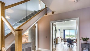 A modern interior with a wooden staircase, a dining area with a view, and a kitchen with a stone accent wall. - 4 bedroom accommodation in Blackwaterfoot (Blackwaterfoot)
