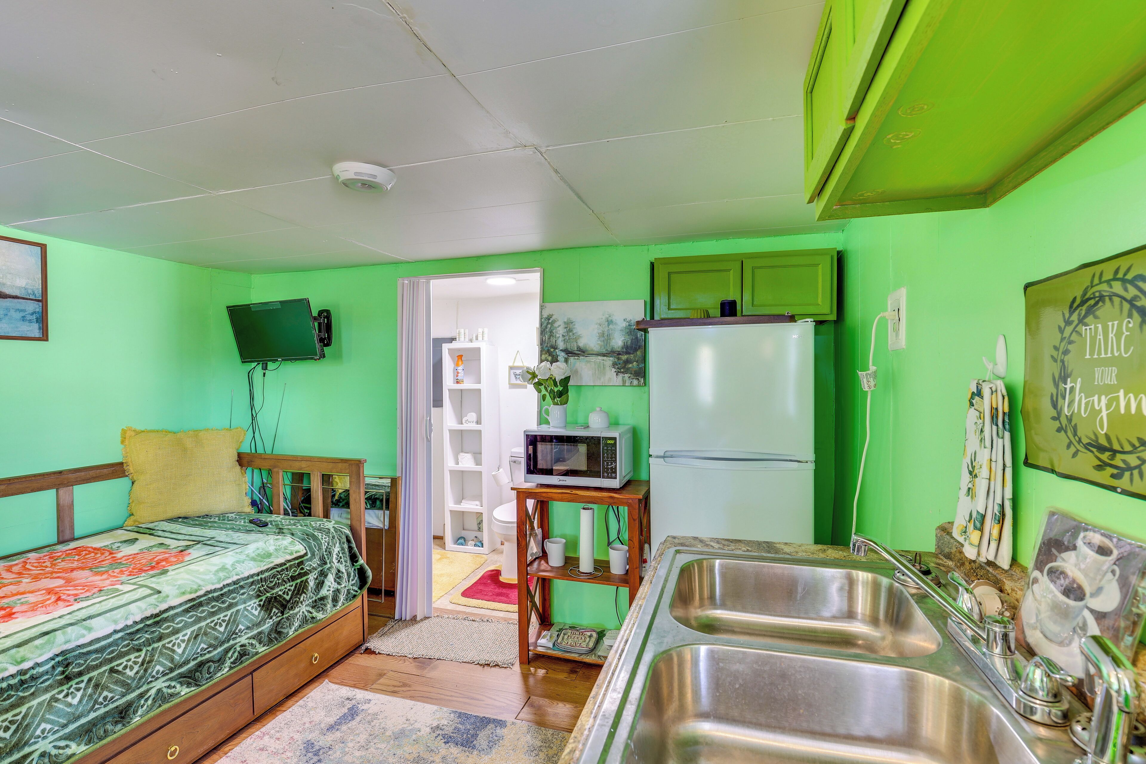 Una habitación pequeña con cama, kitchenette y baño.
