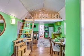 A room with a loft bed, a dining area with a table and chairs, and a kitchen area with a refrigerator and microwave.