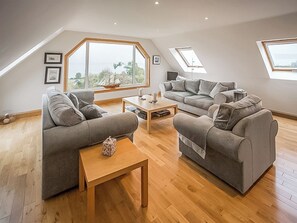 A spacious loft with a high ceiling, large windows offering views of the outdoors, and a modern, neutral color scheme. - 4 bedroom accommodation in Isle of Arran (Isle of Arran)