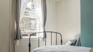 A bedroom with a single bed, a window with curtains, a radiator, and a brick wall visible through the window. - 1 bedroom accommodation in Hebden Bridge (Hebden Bridge)