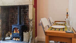 A cozy room with a brick fireplace, a dining table set with plates and glasses, and a basket of firewood. - 1 bedroom accommodation in Hebden Bridge (Hebden Bridge)