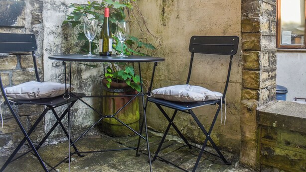 A small outdoor seating area with two chairs and a table, a potted plant, and a bottle of wine. - 1 bedroom accommodation in Hebden Bridge (Hebden Bridge)