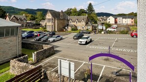 Un espace de stationnement délimité, avec des emplacements réservés aux caravanes et aux voitures, entouré de murs de pierre et de bâtiments à l’architecture traditionnelle.