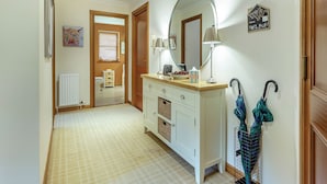 Een hal met een witte dressoir, een spiegel, een lamp en een kapstok met paraplu's.
