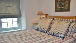 Un letto con biancheria a righe, un comodino con una lampada e un quadro appeso al muro.