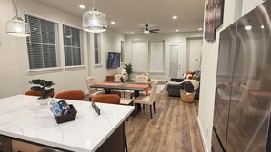 Une cuisine moderne avec un plan de travail en marbre, un coin repas comprenant une table et des chaises, un canapé et un ventilateur de plafond.