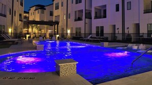 Un espace piscine agrémenté d’un panneau indiquant qu’il est interdit de plonger, entouré d’immeubles à plusieurs étages dotés de balcons et d’un éclairage extérieur.