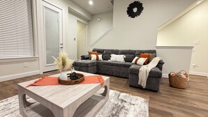 Un salon moderne avec un canapé d’angle, une table basse en bois et un élément décoratif mural.