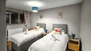Hotellihuone, jossa on kaksi erillistä sänkyä, ikkuna, jossa on verhot, patteri ja yöpöytä, jossa on lamppu.
