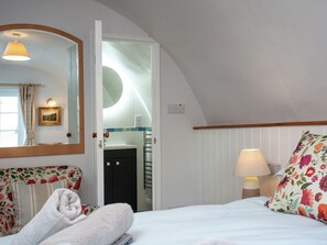 A hotel room with a bed, a bathroom visible through an open door, a mirror, a bedside lamp, and a floral pillow. - Tuckenhay, 1 Castle cottage - FCK (Bow Creek, between Dartmouth and Totnes)