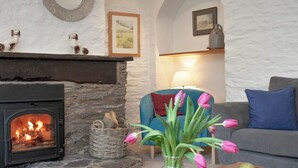 Ein gemütliches Wohnzimmer mit Kamin, einem blauen Sessel, einer Blumenvase und einer Schale Birnen.