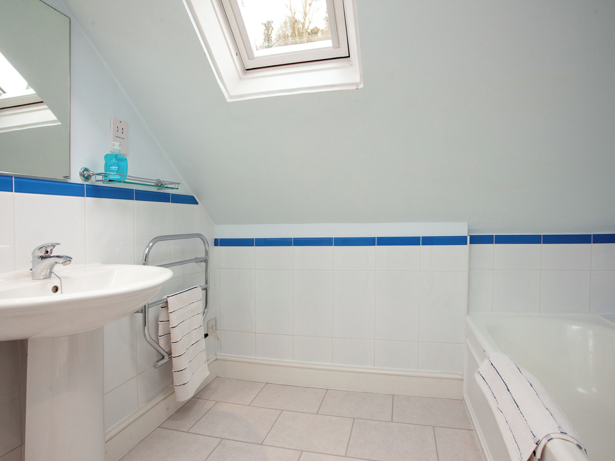 A bathroom with a skylight, a sink, a bathtub, and a towel rack.