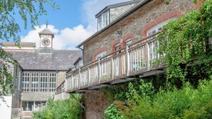 Un edificio storico con una torre dell'orologio, pareti in pietra e un balcone con ringhiera in legno.