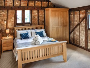 A wooden bed with rolled towels, pillows, and a plate of croissants in a room with exposed brick walls and wooden beams.