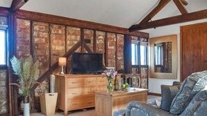 Une pièce avec des poutres apparentes, un mur en briques, une commode en bois, un téléviseur, un canapé et une fenêtre.