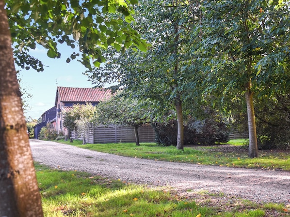 A gravel driveway leading to a house with a red-tiled roof, surrounded by trees and a wooden fence.