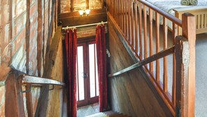 Un escalier en bois avec une rampe, des marches recouvertes de moquette et des rideaux rouges.