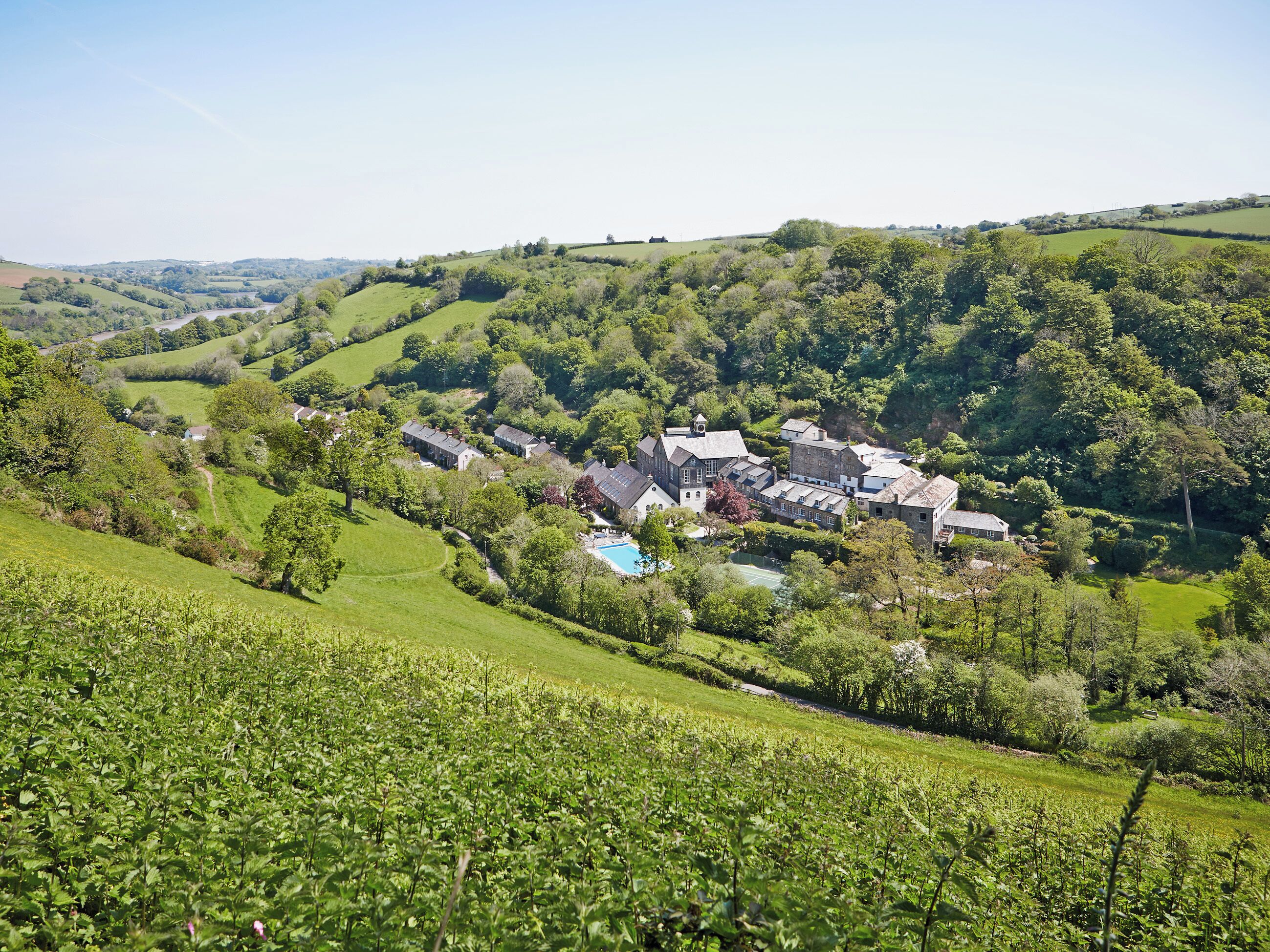 A rural landscape with rolling hills, a swimming pool, and a cluster of traditional buildings.