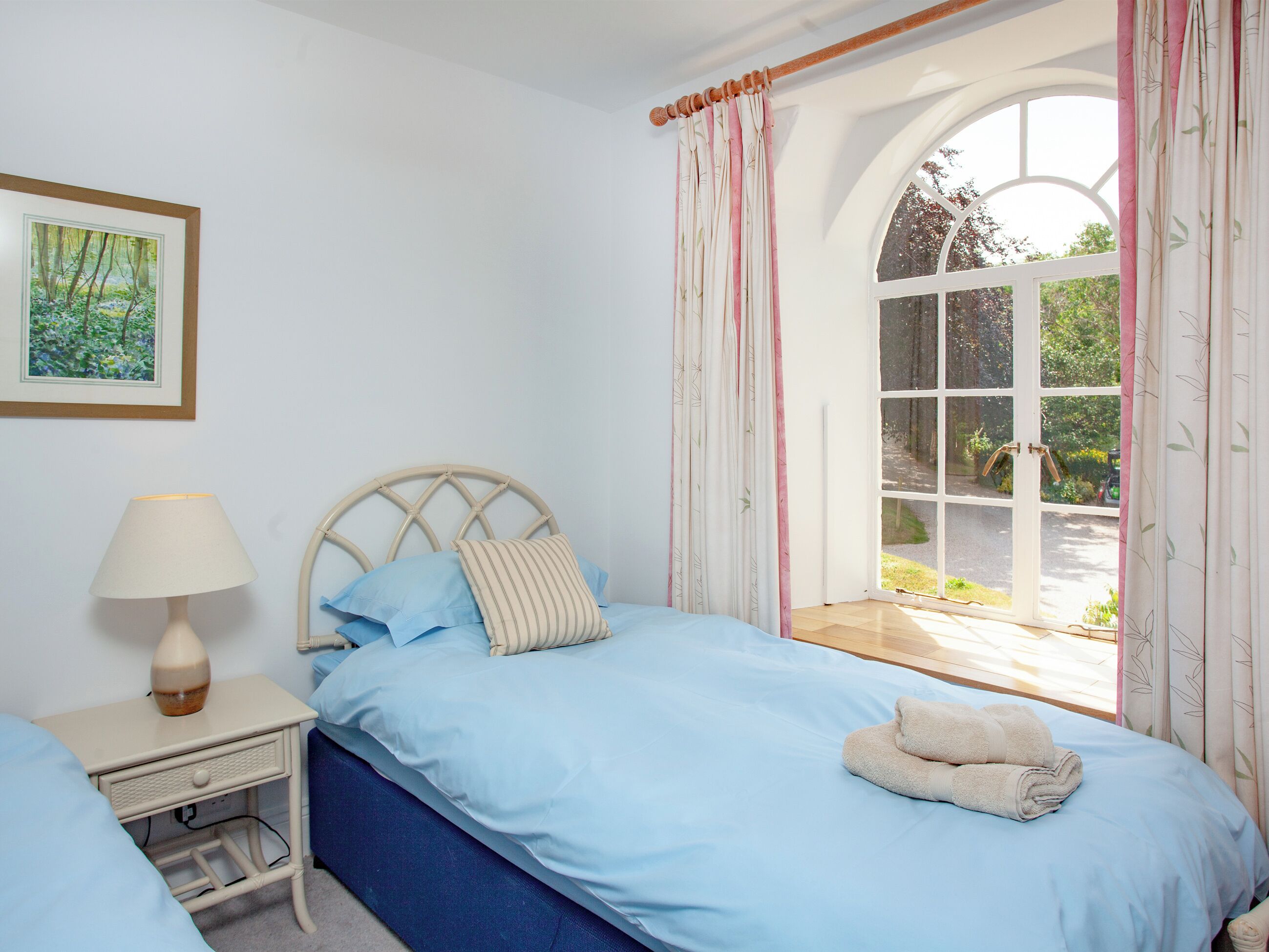 A bedroom with a bed, a nightstand, a lamp, a window with curtains, and a framed picture on the wall.