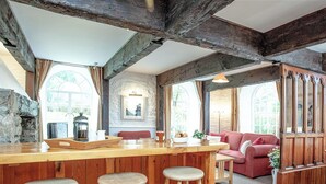 Ein rustikales Interieur mit freiliegenden Holzbalken, einer Bar mit Hockern, einem roten Sofa und einer Steinwand.