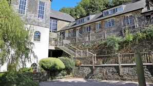 A stone building with multiple windows and a staircase leading to a balcony. - Tuckenhay, Clock Tower Cottage - FJG (Bow Creek, between Dartmouth and Totnes)
