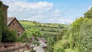 A stone cottage with a wooden fence, a garden, and a view of rolling hills. - Tuckenhay, Papermaker's - FKE (Bow Creek, between Dartmouth and Totnes)