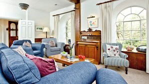 A living room with a sofa, armchair, wooden piano, and large windows. - Tuckenhay, Papermaker's - FKE (Bow Creek, between Dartmouth and Totnes)