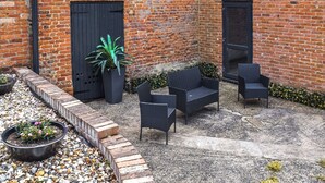 A brick building with two black doors, outdoor wicker furniture, and a potted plant. - Sunflower Bungalow - UK50569 (Little Dunham, near Kings Lynn)
