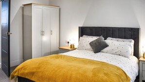 A bedroom with a bed, a wardrobe, a bedside table with a lamp, and a nightstand. - Sunflower Bungalow - UK50569 (Little Dunham, near Kings Lynn)