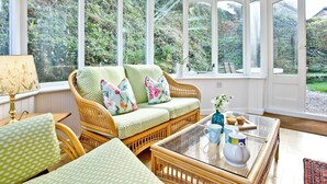 Une véranda meublée de mobilier en osier, avec une table basse en verre et une vue sur la verdure.