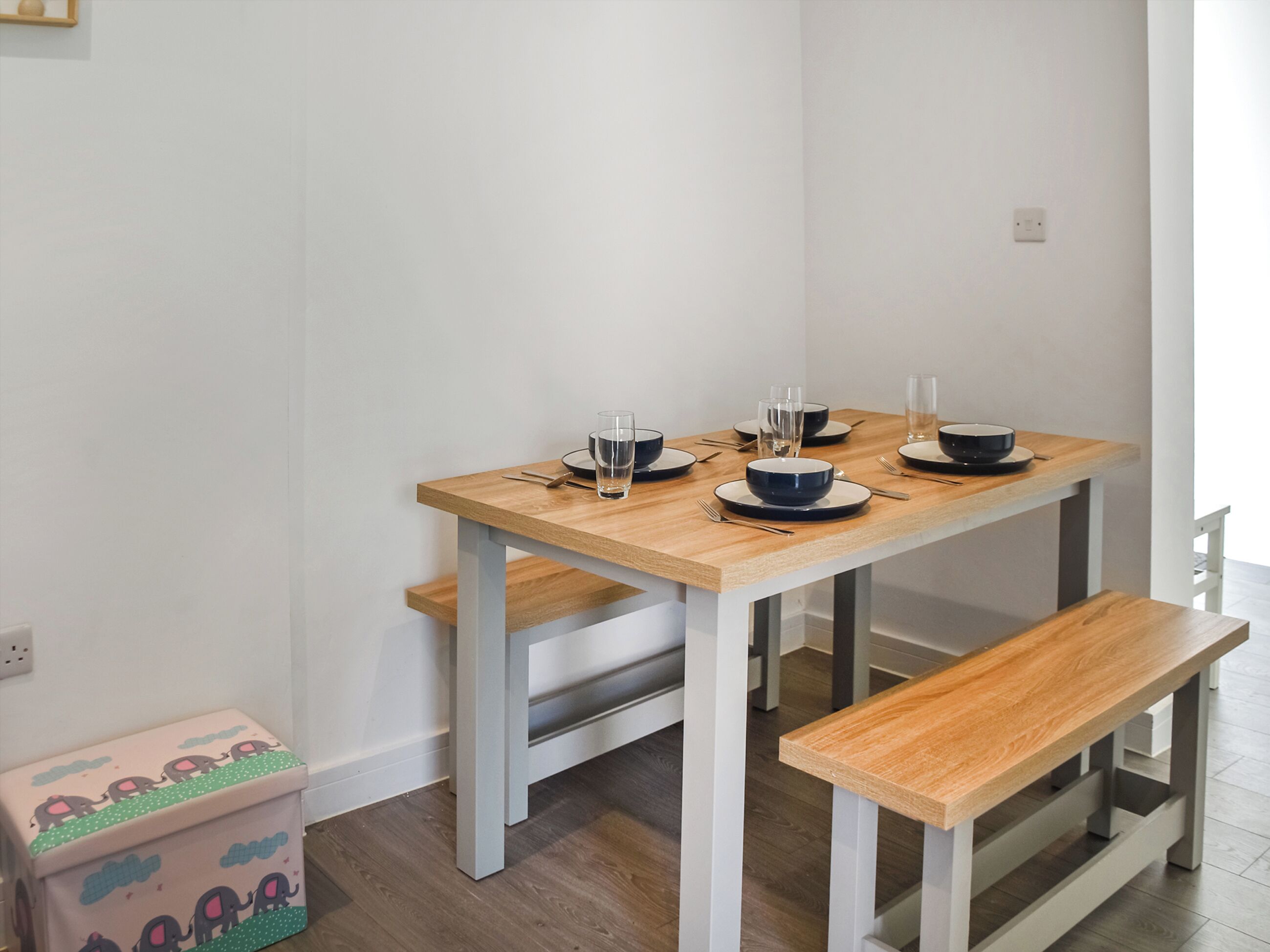 A dining table with benches, a wooden floor, and a small storage box with elephant designs.