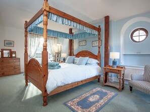 A four-poster bed with a canopy, a nightstand, a chair, and a round window. - Tuckenhay, Mill House - FUB (Bow Creek, between Dartmouth and Totnes)