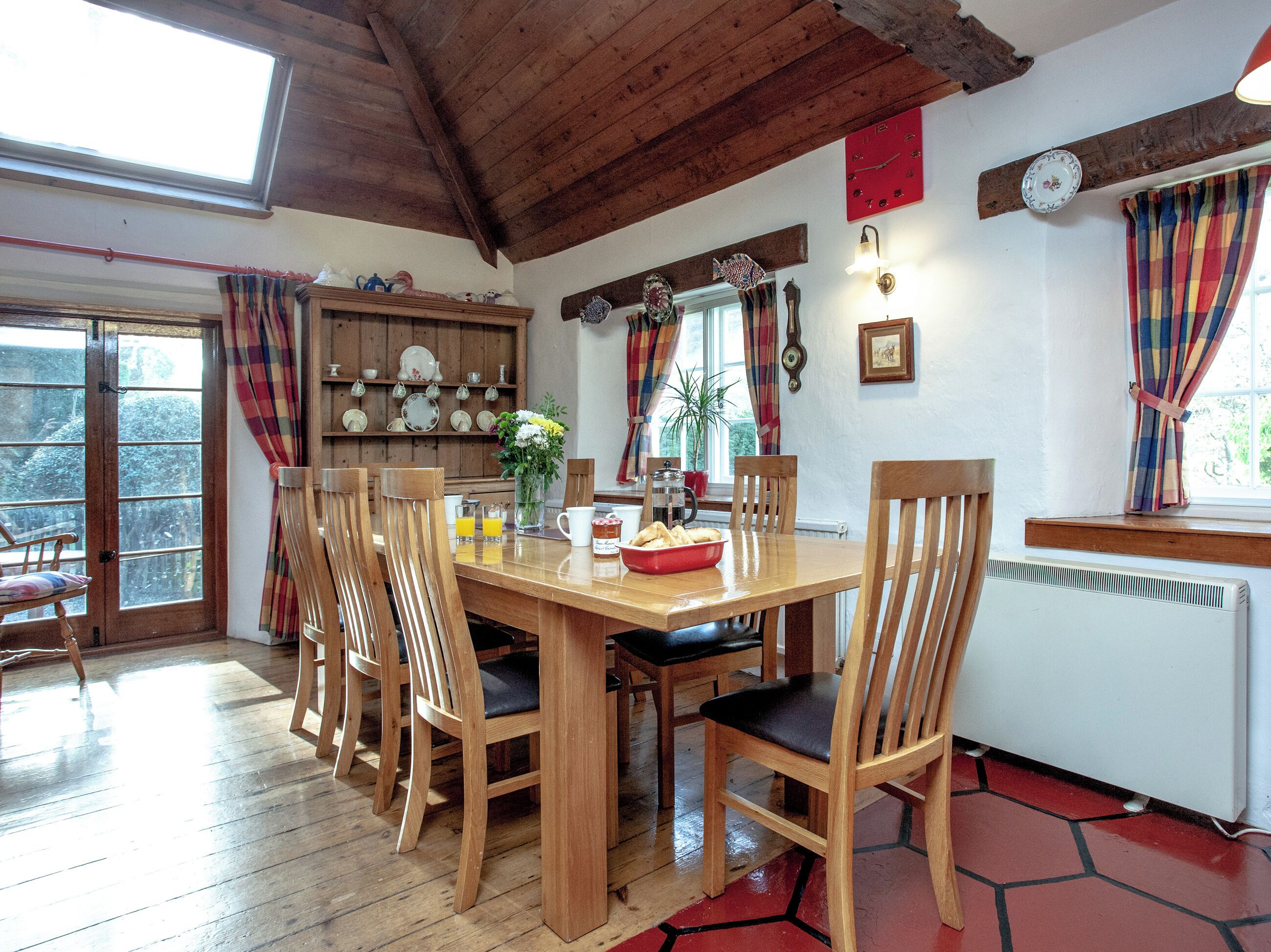 A wooden dining table with chairs, a red clock, and a window with curtains.