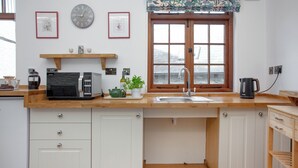 A kitchen with white cabinets, a wooden countertop, a coffee machine, a kettle, and a window with a floral valance.