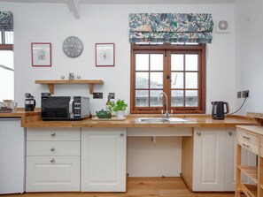 Eine Küche mit weißen Schränken, einer Holzarbeitsplatte, einer Kaffeemaschine, einem Wasserkocher und einem Fenster mit Blumenrollo.