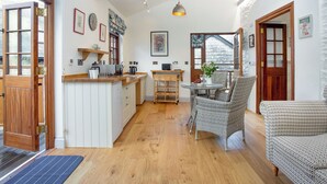 A cozy kitchen with wooden cabinets, a dining area with wicker chairs, and a large window providing natural light.