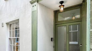 Une porte verte avec un panneau en verre dépoli, une petite fenêtre avec un cadre blanc et un luminaire fixé au mur.